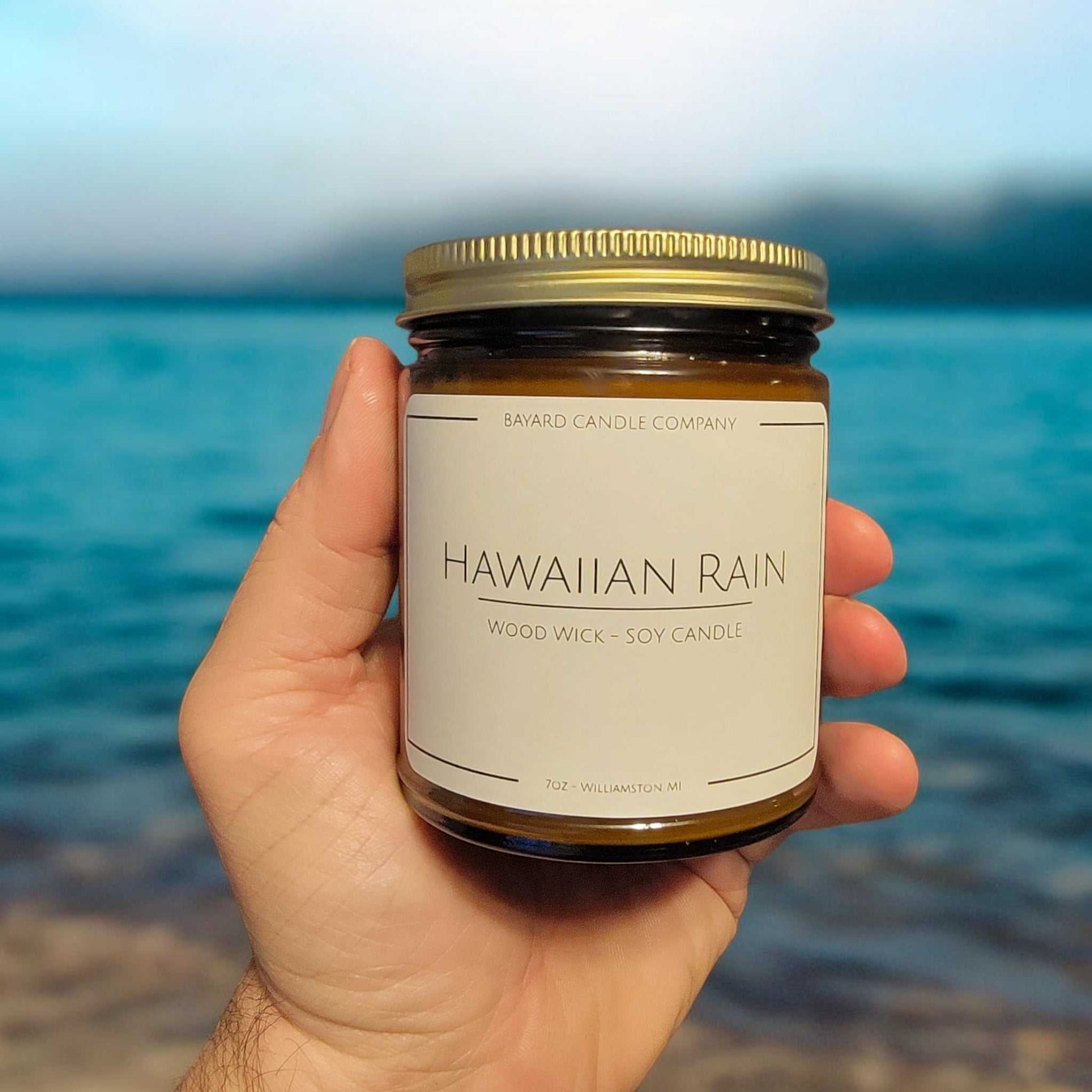 Hawaiian Rain Wood Wick Candle in a hand by tropical water 